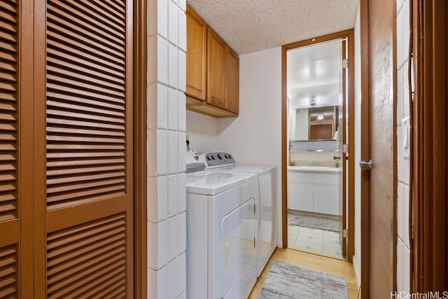 washroom with cabinets, washer and dryer, a textured ceiling, light wood-type flooring, and sink