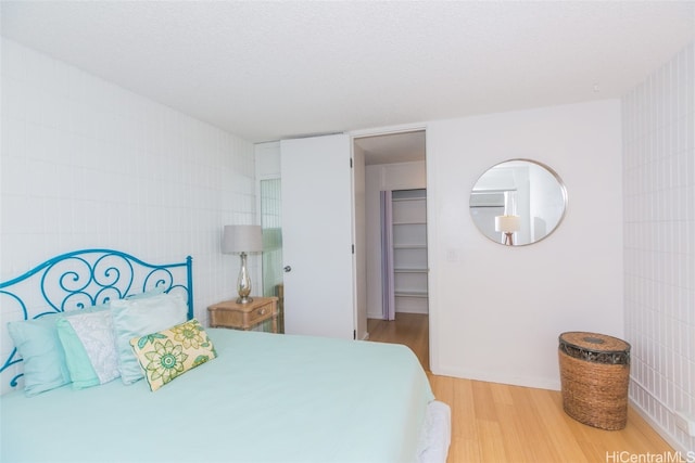 bedroom featuring a walk in closet, tile walls, a textured ceiling, wood-type flooring, and a closet