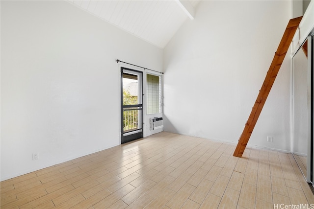 empty room with beamed ceiling, light hardwood / wood-style floors, and high vaulted ceiling