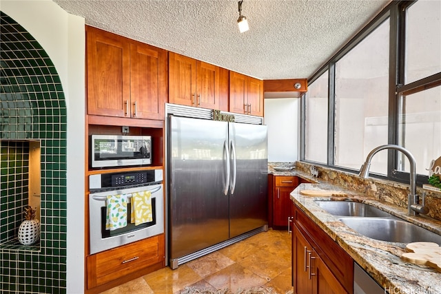 kitchen with sink, a textured ceiling, stainless steel appliances, tile walls, and light stone counters