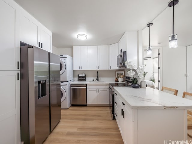 kitchen featuring appliances with stainless steel finishes, sink, light wood-type flooring, stacked washer / dryer, and white cabinetry