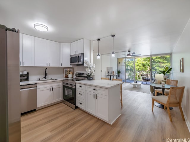 kitchen featuring white cabinetry, stainless steel appliances, kitchen peninsula, and hanging light fixtures