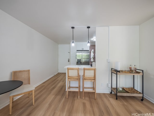 kitchen with stainless steel fridge, kitchen peninsula, pendant lighting, and light hardwood / wood-style floors