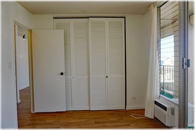 unfurnished bedroom featuring a closet, light hardwood / wood-style flooring, a wall unit AC, and multiple windows