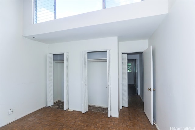 unfurnished bedroom featuring dark parquet flooring, multiple closets, a high ceiling, and multiple windows