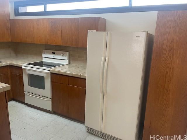 1088 Bishop St Unit 1213, Honolulu, HI 96813 - kitchen with white appliances, tile countertops, brown cabinets, and backsplash