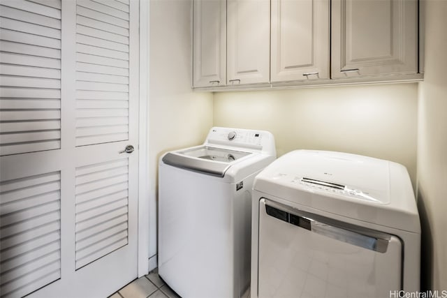 clothes washing area with light tile patterned floors, cabinets, and separate washer and dryer