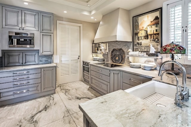 kitchen featuring gray cabinetry, tasteful backsplash, appliances with stainless steel finishes, sink, and premium range hood