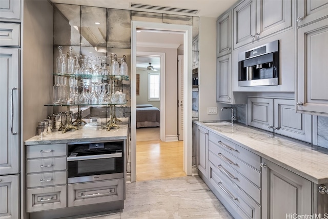 kitchen with sink, light stone countertops, appliances with stainless steel finishes, light hardwood / wood-style floors, and ceiling fan