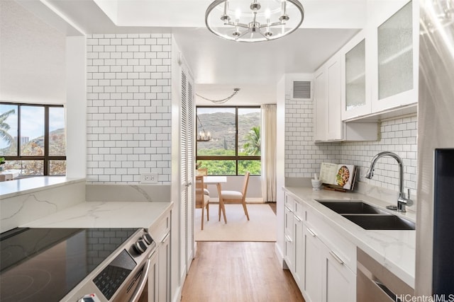 kitchen with a mountain view, sink, white cabinets, light stone counters, and light hardwood / wood-style flooring