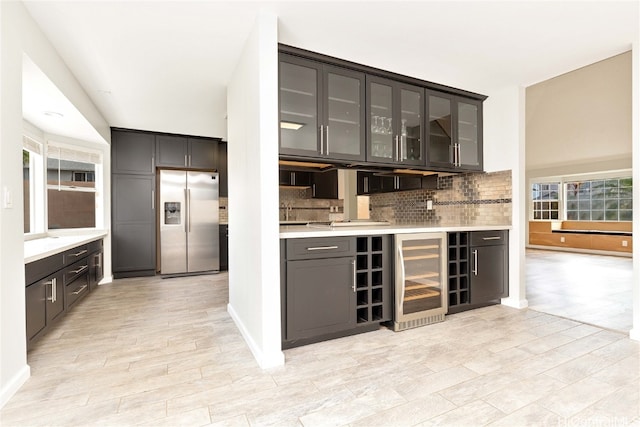 bar featuring stainless steel refrigerator with ice dispenser, dark brown cabinets, backsplash, beverage cooler, and light hardwood / wood-style floors