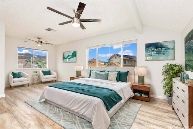 bedroom with ceiling fan, a textured ceiling, light wood-type flooring, and vaulted ceiling with beams