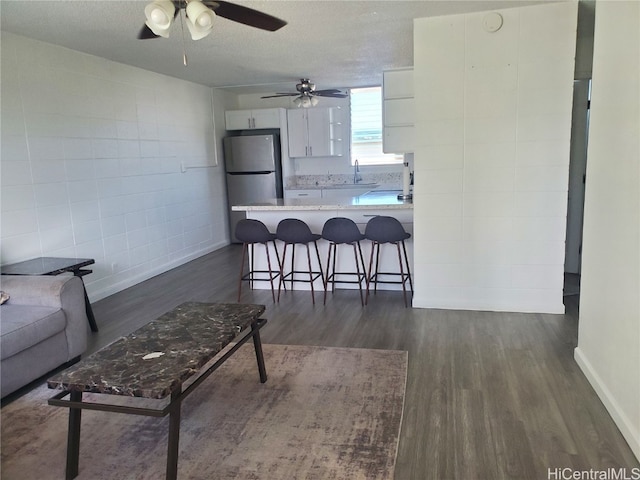 kitchen with a textured ceiling, kitchen peninsula, stainless steel fridge, white cabinets, and dark hardwood / wood-style floors