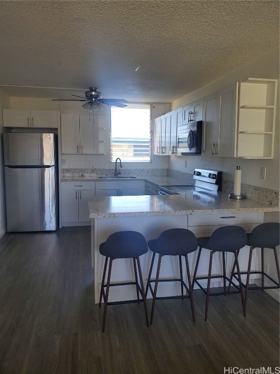 kitchen with kitchen peninsula, a breakfast bar area, appliances with stainless steel finishes, white cabinetry, and dark hardwood / wood-style floors