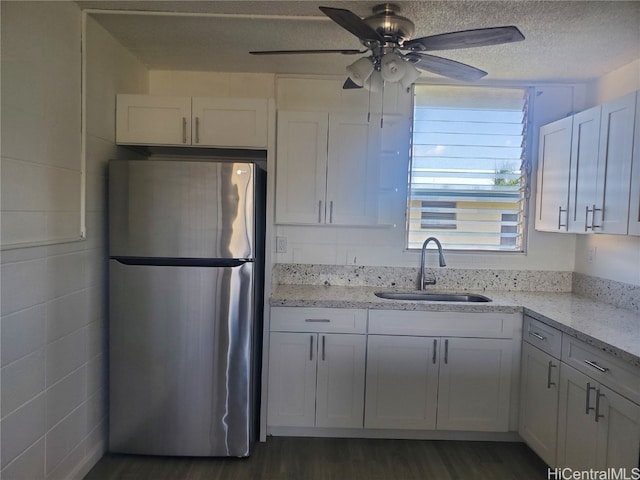 kitchen featuring white cabinets, light stone counters, a textured ceiling, stainless steel refrigerator, and sink