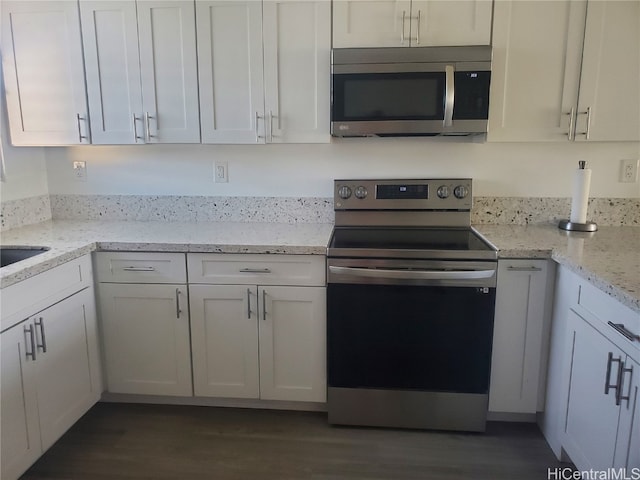 kitchen with appliances with stainless steel finishes, white cabinets, light stone counters, and dark wood-type flooring