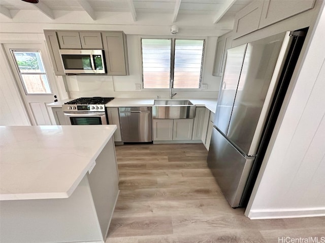 kitchen with beam ceiling, stainless steel appliances, sink, and light wood-type flooring