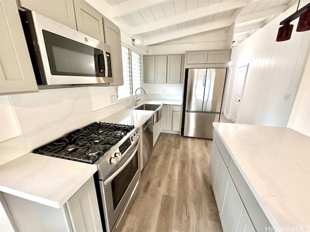 kitchen with gray cabinetry, sink, light wood-type flooring, lofted ceiling with beams, and stainless steel appliances