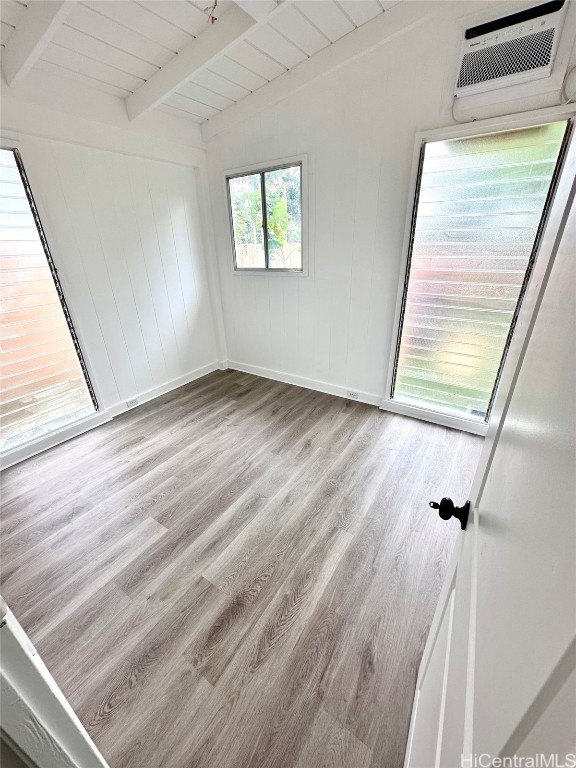 unfurnished room featuring a wall unit AC, wooden ceiling, light wood-type flooring, wood walls, and lofted ceiling with beams