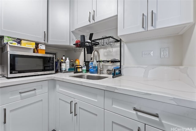 kitchen with light stone counters, sink, and white cabinets