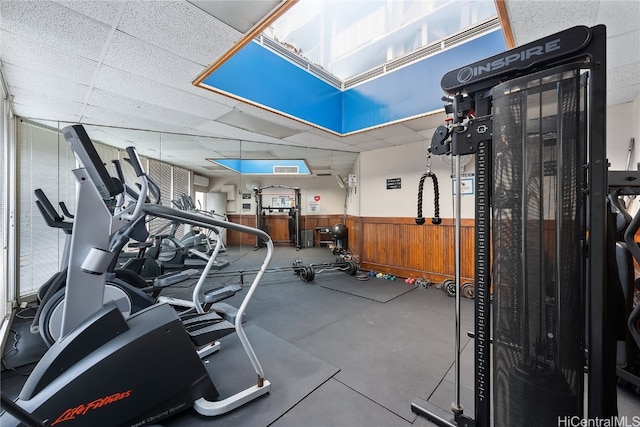 exercise room with a drop ceiling and wooden walls