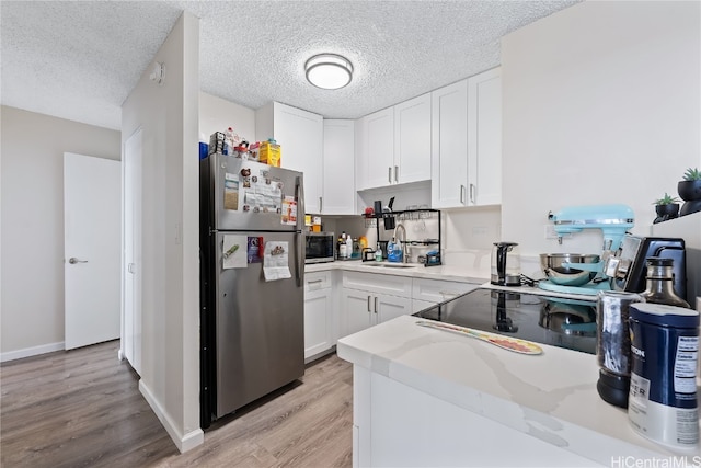 kitchen with white cabinets, a textured ceiling, light wood-type flooring, stainless steel appliances, and light stone counters