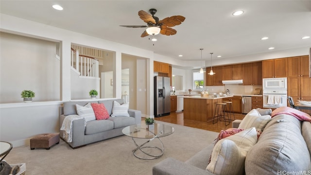 living room with light wood-type flooring, ceiling fan, and sink