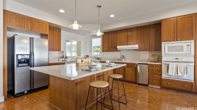 kitchen with pendant lighting, white appliances, dark hardwood / wood-style floors, a kitchen island, and a breakfast bar area