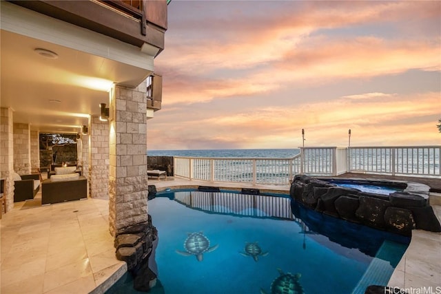 pool at dusk with an in ground hot tub, a water view, and a patio area