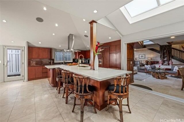 kitchen featuring island range hood, sink, vaulted ceiling with skylight, a breakfast bar, and a large island with sink