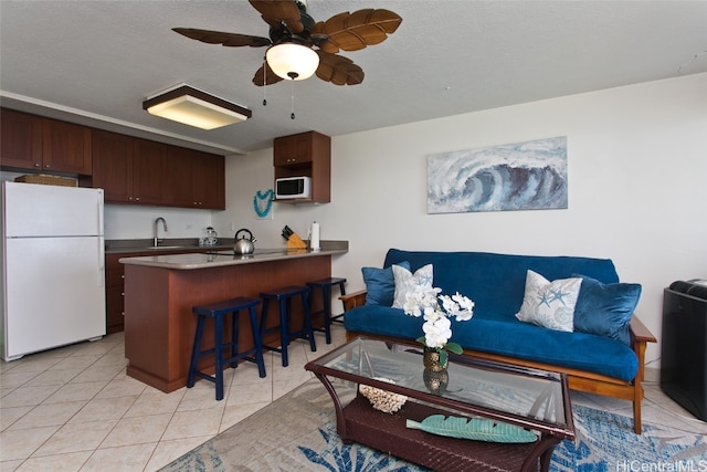 kitchen featuring white appliances, light tile patterned floors, a kitchen breakfast bar, a peninsula, and a sink