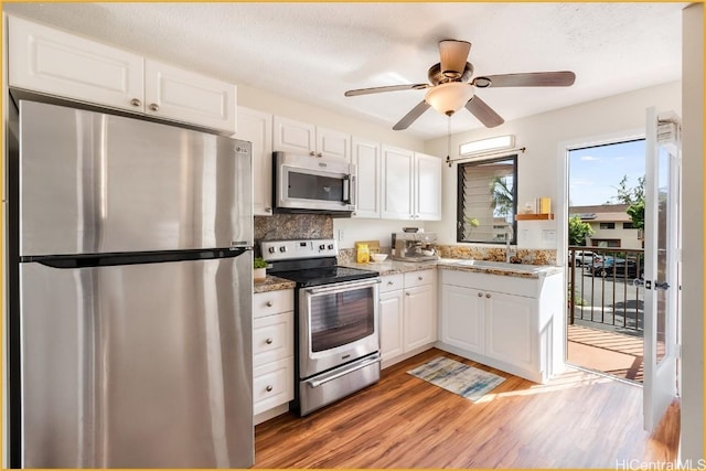 kitchen featuring white cabinetry, stainless steel appliances, light stone counters, light hardwood / wood-style flooring, and decorative backsplash