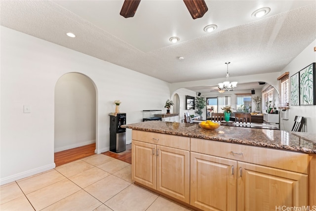 kitchen with dark stone counters, ceiling fan with notable chandelier, light tile patterned floors, a textured ceiling, and decorative light fixtures