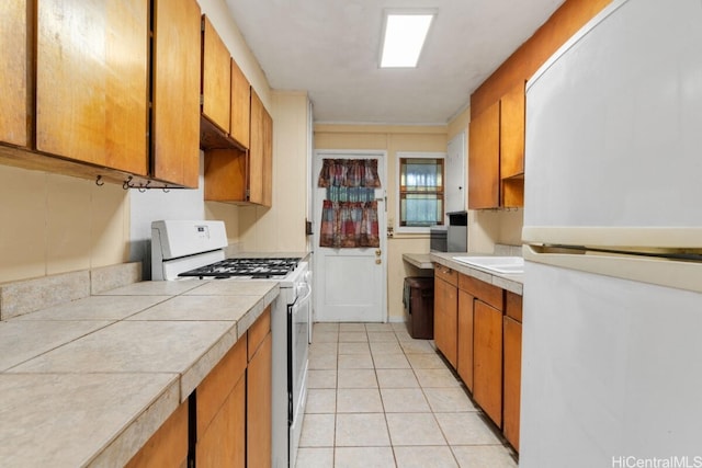 kitchen featuring tile countertops, sink, light tile patterned floors, and white appliances