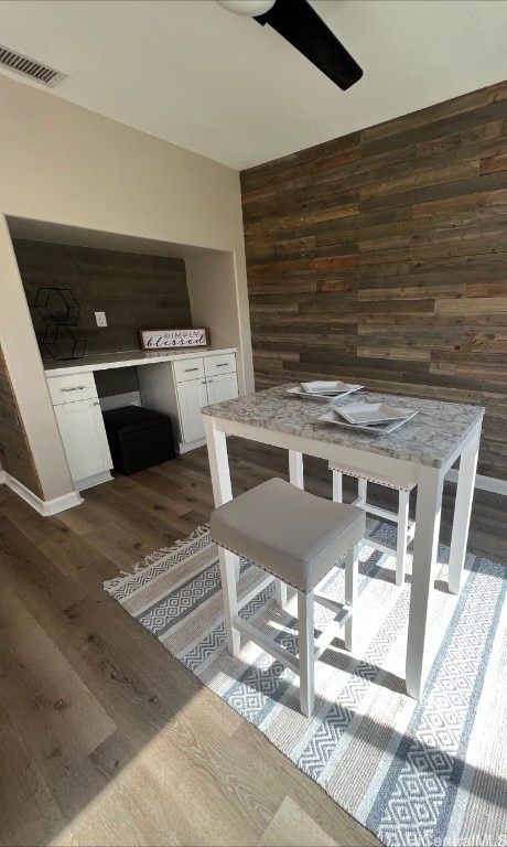 unfurnished dining area featuring dark wood-type flooring, ceiling fan, and wood walls