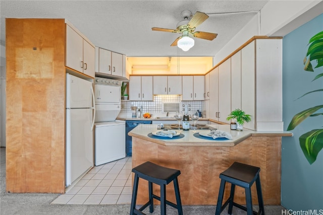 kitchen featuring white cabinets, black dishwasher, a breakfast bar area, stacked washer / drying machine, and white fridge