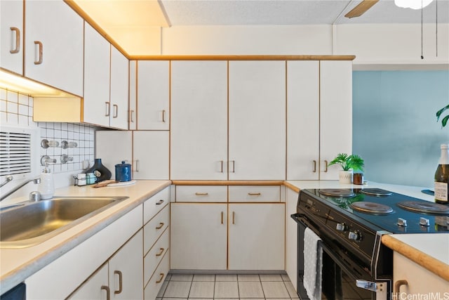 kitchen featuring decorative backsplash, sink, black / electric stove, light tile patterned floors, and white cabinets