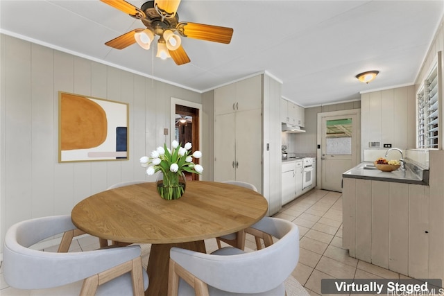 dining room featuring sink, ceiling fan, light tile patterned floors, crown molding, and wooden walls