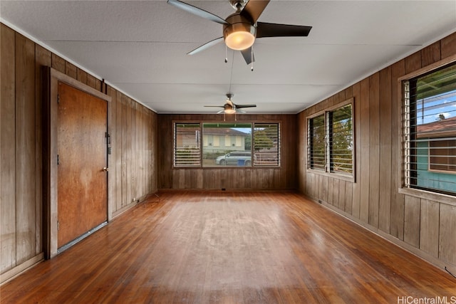 empty room with wooden walls, hardwood / wood-style floors, and a healthy amount of sunlight