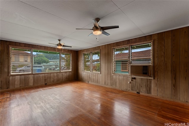 unfurnished room with wooden walls, wood-type flooring, and ceiling fan