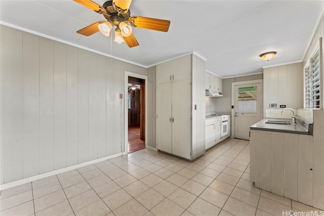 kitchen with wooden walls, sink, ceiling fan, light tile patterned flooring, and white cabinetry