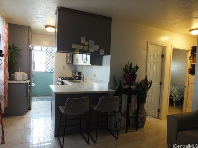 kitchen featuring kitchen peninsula, a textured ceiling, stainless steel appliances, and a breakfast bar area