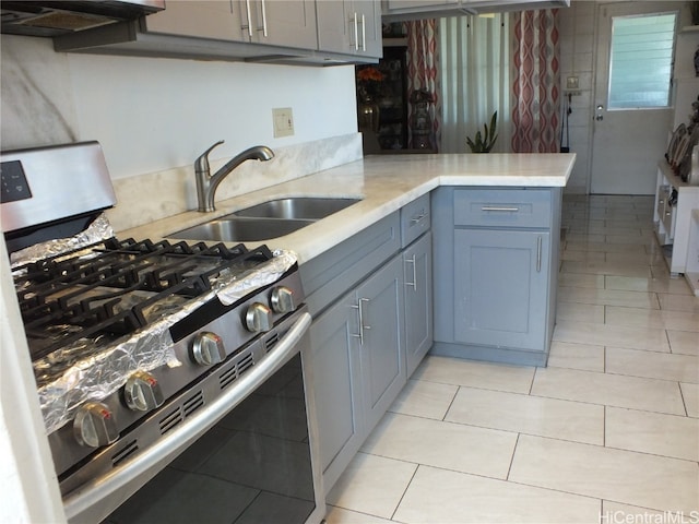 kitchen with gas range, kitchen peninsula, sink, and light tile patterned floors