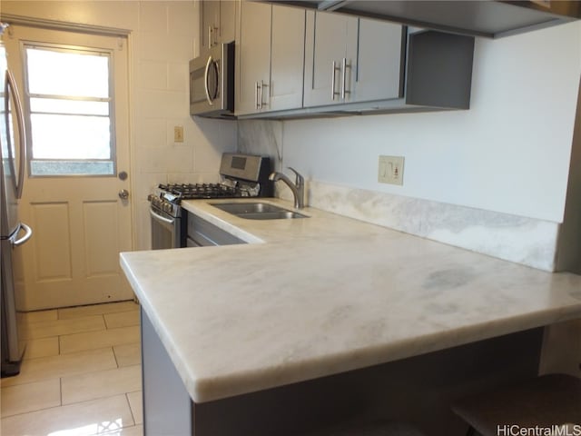 kitchen featuring sink, kitchen peninsula, stainless steel appliances, gray cabinets, and decorative backsplash