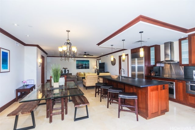 interior space featuring wall chimney range hood, tasteful backsplash, a kitchen island with sink, sink, and stainless steel appliances