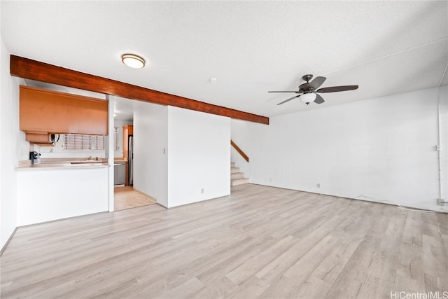 unfurnished living room with beamed ceiling, a textured ceiling, light hardwood / wood-style floors, and ceiling fan