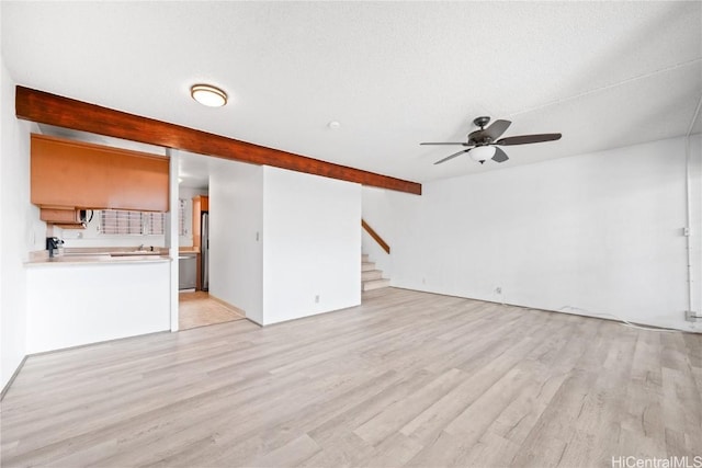 unfurnished living room featuring ceiling fan, beamed ceiling, stairway, and light wood-style flooring