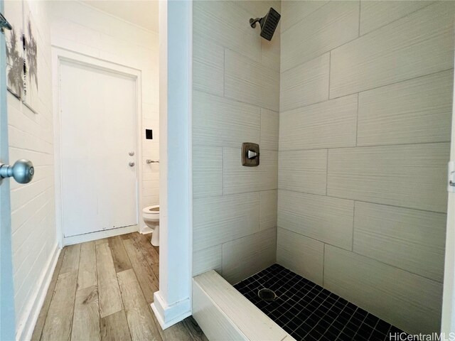 bathroom with toilet, hardwood / wood-style flooring, a shower, and tile walls