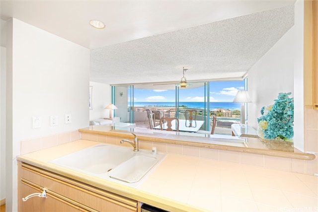 kitchen with a water view, tile countertops, a textured ceiling, and sink