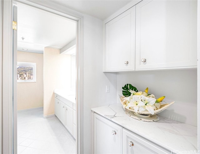 bar with light stone counters, light tile patterned flooring, and white cabinets